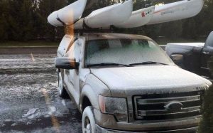 Snow on truck with kayaks on rack.