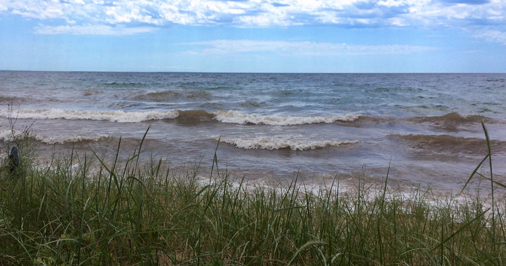 Northern Lake Michigan near Seul Choix Lighthouse. View of grassy beach and rough waters with a blue sky.